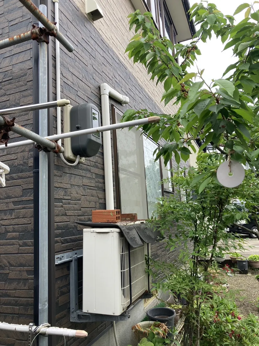 酒田市 エアコン交換前 室外機（経年使用・上に重しのブロックを置いた状態）